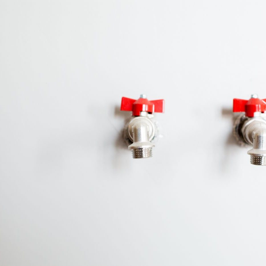 Two outdoor hose bibs with red handles on a finished wall